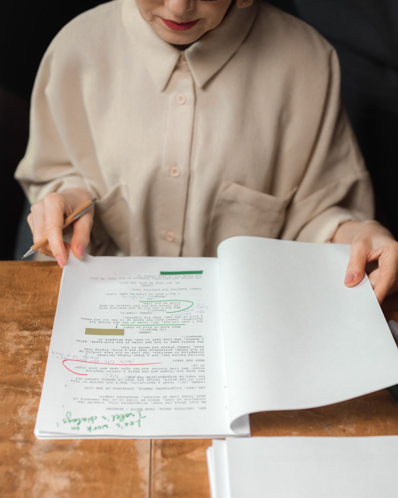 An editor turning the pages of a printed manuscript covered in handwritten corrections at a wooden desk